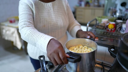Obraz na płótnie Canvas A senior African woman cooking pasta at home stirring pot casual real life