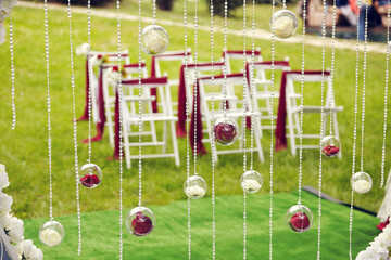 Decorated white chairs outdoor on green grass. Curtain of beads and glass balls with flowers