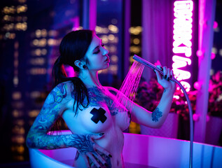 naked sexy girl with tattoos bathing in a bathtub with a view of the lights of the big city in neon...