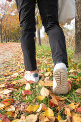 Feet sneakers walking on fall leaves in park with Autumn season nature.