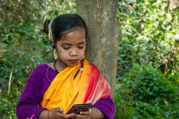 A tribal little girl is listening to music with Bluetooth headphones on her android phone.