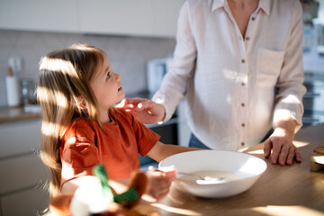 Little girl having breakfast with mother in kitchen.