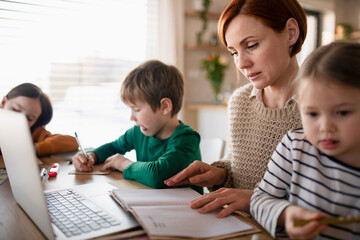 Mother of little children working on laptop when distance learning and doing artwork at home.
