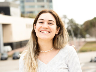  Smiling blonde young woman looking at camera in a city. Positive emotions