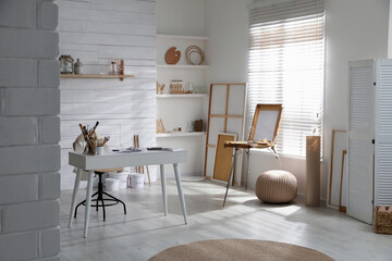 Modern studio interior with artist's workplace and wooden easel near large window