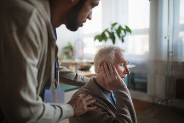 Caregiver helping seniot man to insert hearing aid in his ear.