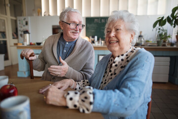 Smiling elderly woman and man enjoying breakfast in nursing home care center.