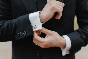 A man in a black suit straightens his sleeves A man buttoning a white jacket Groom getting ready in the morning before the wedding ceremony Groom adjusting his cufflinks Close up