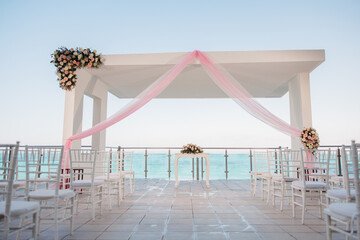 Wedding ceremony and reception place, a white arch decorated with pink cloth and colorful flowers Sea view at the background White Wedding chairs and wedding arch on the terrace Isolated