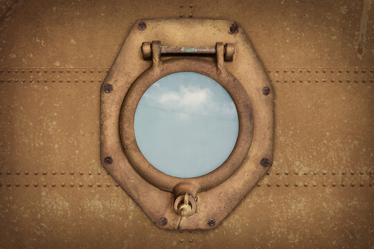 Ancient rusted ship porthole with view at a blue sky