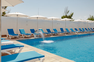 view of the pool with blue water, sun loungers and umbrellas