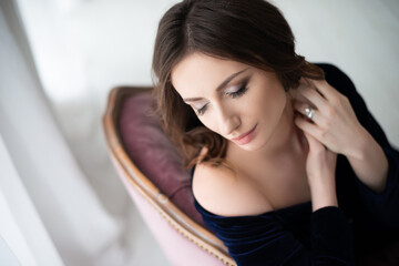 A beautiful brunette girl in an elegant velvet dress sits on an antique baroque armchair