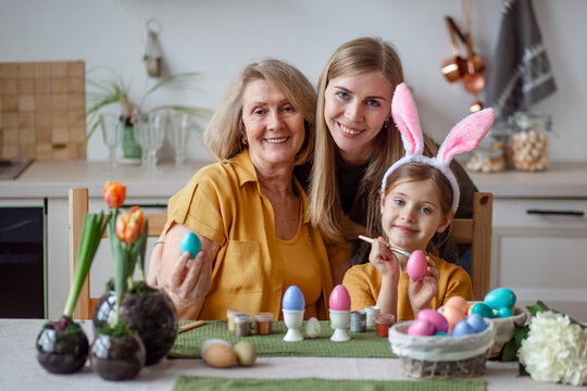 Happy easter family elderly grandmother and young woman mother blonde with little daughter with rabbit ears are preparing for the holiday to paint eggs