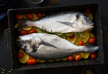 Fish in a baking sheet with potatoes and tomatoes, ready to bake