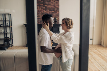 Young african man embraces his caucasian pregnant woman and touches her belly.