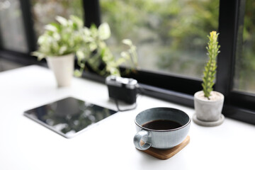 Blue coffee cup and tablet and plants in front of window