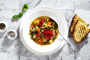 summer italian minestrone soup with tomatoes and homemade bread on a marble table