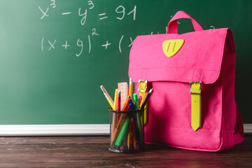 Stylish backpack and holder with stationery on table in classroom