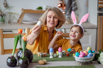 Happy easter family elderly grandmother and little granddaughter with rabbit ears are preparing for the holiday to paint eggs