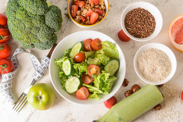 Composition with bowl of fresh salad, healthy products and measuring tape on light background
