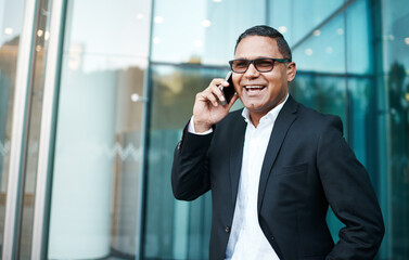 Ive just stepped out. Cropped shot of a handsome mature businessman making a phonecall with his office in the background.