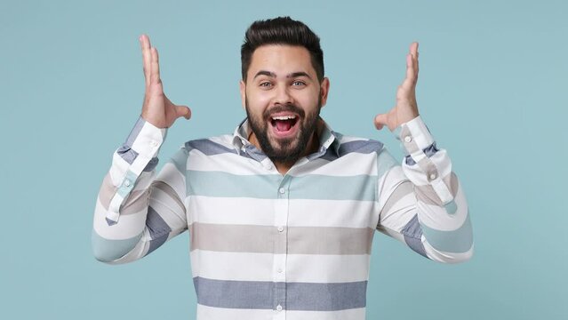 Cheerful fun young bearded brunet man 20s years old wears striped shirt showing mind explosion gesture isolated on plain pastel light blue background studio portrait. People emotions lifestyle concept