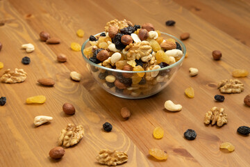 Delicious and healthy snack walnuts, cashews, hazelnuts and raisins are poured into a transparent bowl on a wooden table close-up