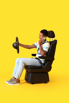 African-American Man In Car Seat And With Steering Wheel Talking By Phone On Color Background