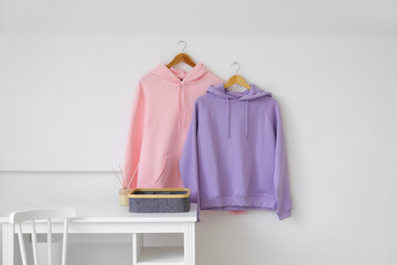 Table with organizer and stylish hoodies hanging on light wall