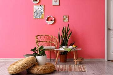 Interior of room with comfortable chair, table and stylish decor near color wall
