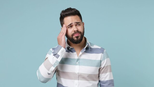 Tired sad sullen young bearded brunet man 20s wear striped shirt did not get enough sleep last night barely got up in the morning yawning isolated on plain pastel light blue background studio portrait