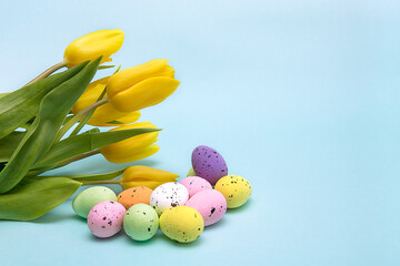 Easter colorful eggs on a blue background with a bouquet of yellow tulips, Easter greeting card with space for text