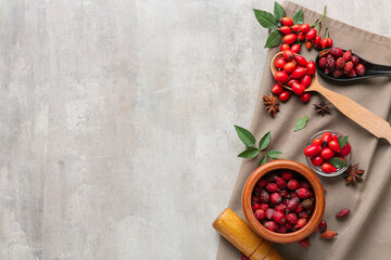Mortar and spoons with rose hip berries on light background