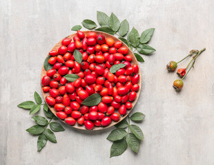 Plate with fresh rose hip berries on light background