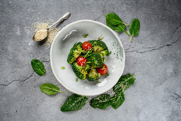 Vegetarian salad with broccoli, tomatoes, feta cheese, and pumpkin on a blue ceramic plate on a black concrete background, side view, close up,