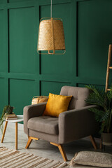 Soft armchair and hanging lamp near green wall