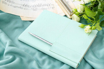 Stylish notebook with note sheets and roses on color fabric background, closeup