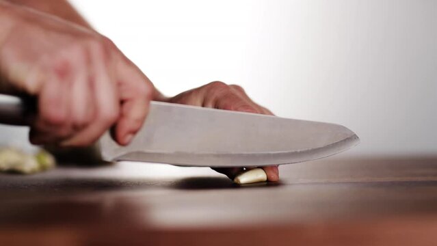 Professional chef cutting garlic on wood chopping block.