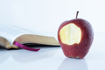 Red bitten apple with an open Holy Bible Book on white background. The Christian biblical concept...