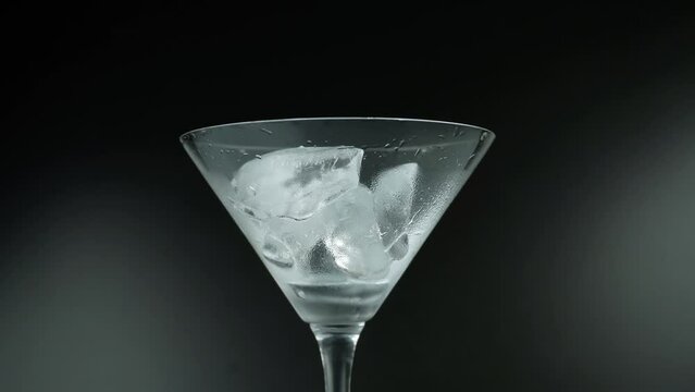 Putting ice cubes in a empty martini glass filling up with absinthe isolated on black background
