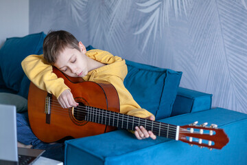 Handsome kid dressed casual jeans and yellow sweatshirt watches video lesson on playing the guitar...