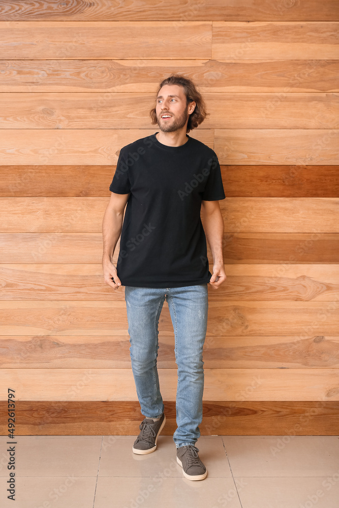 Wall mural Handsome young man in black t-shirt on wooden background