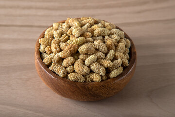 Bowl full of dried mulberry on a wooden background	