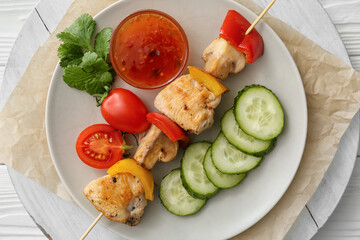 Plate of grilled chicken skewers with vegetables and sauce on table