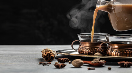 Indian masala chai tea. Hot masala chai spiced tea with milk and spices is poured into a glass glass on dark background. Long banner format. place for text