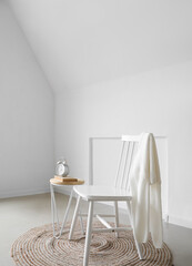 Modern table with alarm clock, books and chair in interior of light room