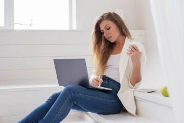 A young girl is sitting in an office in an informal setting with a laptop in her hands.