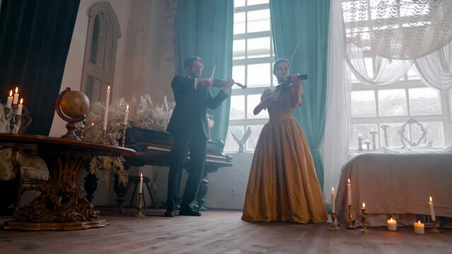 A Young Girl And Man Plays The Violin In A Beautiful Retro Room With Flowers And A Piano. 