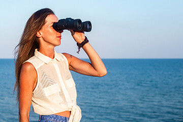 Young woman looking through binoculars at sea from cliff.