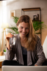 Girl holding a glass of water. Smiling girl drinking water while using the laptop..